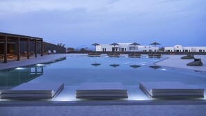 Un área de piscina moderna con sillas de descanso y sombrillas, una piscina cristalina y un edificio al fondo.