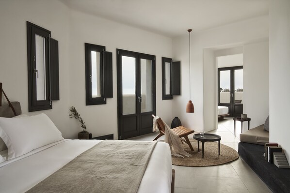 A modern hotel room with a large bed, a seating area with a small table, and a view of the outdoors through the door.