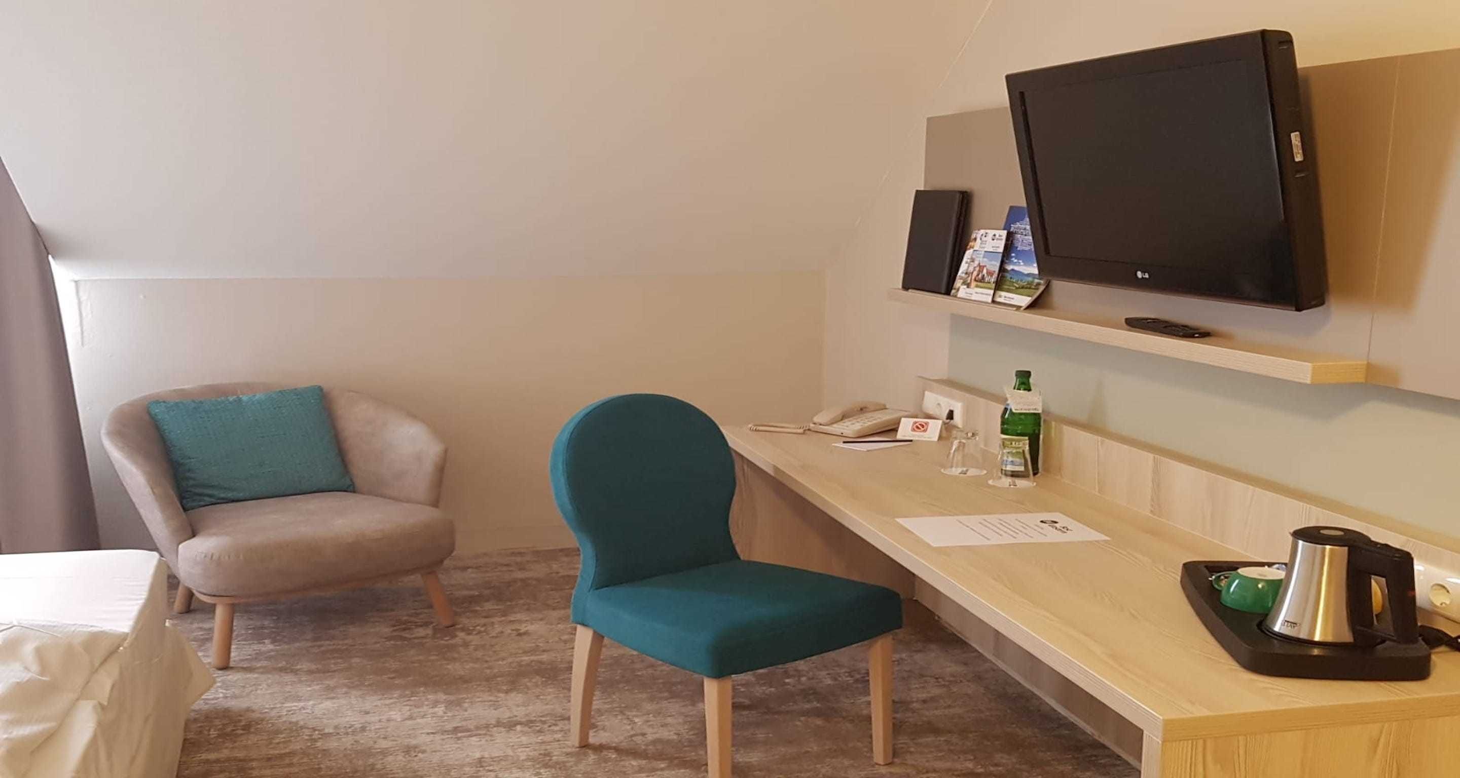 Hotellihuone, jossa on sänky, työpöytä, puhelin, televisio ja pehmustettu tuoli.