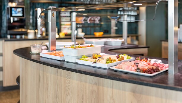 A buffet counter with various food items and a television screen in the background.