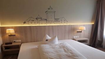 A hotel room with a large bed, two bedside tables, a wall-mounted lamp, and a wall art depicting a castle.