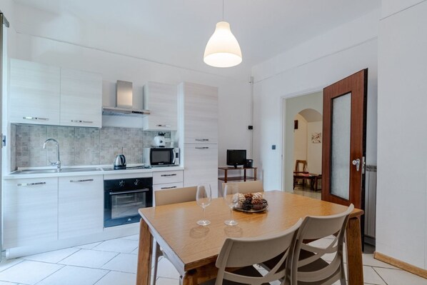 A modern kitchen with white cabinets, a dining table with chairs, and a pendant light.