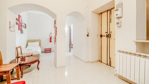 Habitación de hotel con cama, una mesa de comedor de madera, sillas, un sofá rojo y un pasillo con un arco.