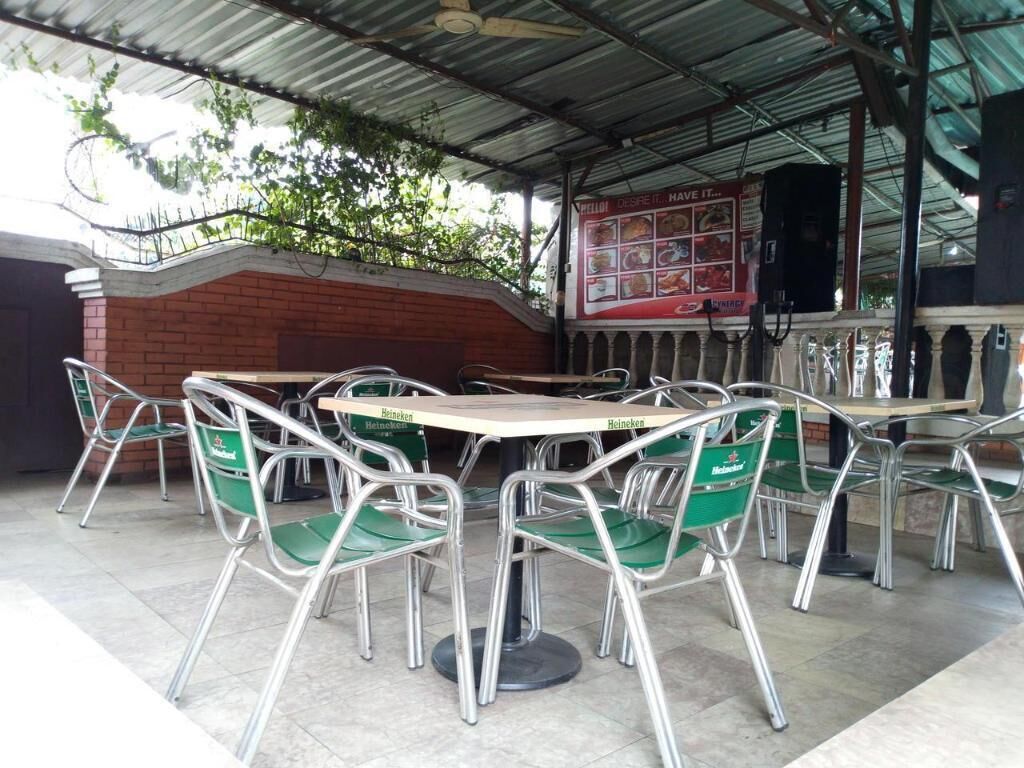 Zona salotto esterna riparata, con tavoli e sedie in metallo, un muro in mattoni e una bacheca con il menu.