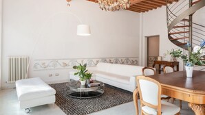 Een moderne woonkamer met een witte bank, een ronde salontafel met planten, een kroonluchter en een spiltrap.
