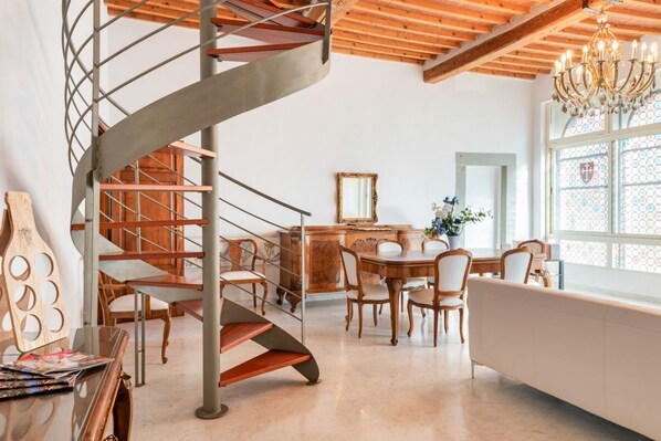 A modern interior with a spiral staircase, wooden dining table, chairs, and a chandelier.