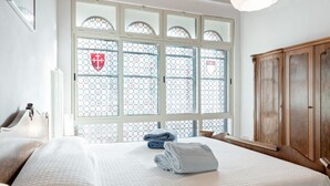 Een hotelkamer met een groot raam, een bed met een witte quilt, een houten garderobe en een hoofdeinde.