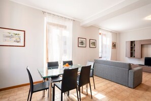 Un salon moderne avec une table à manger en verre, un canapé gris et un téléviseur posé sur un meuble en bois.