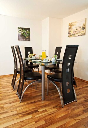 A dining area with a glass table, four black chairs, and two wall-mounted paintings. - Holiday home Findling Summer - House Findling (Sankt Lambrecht)