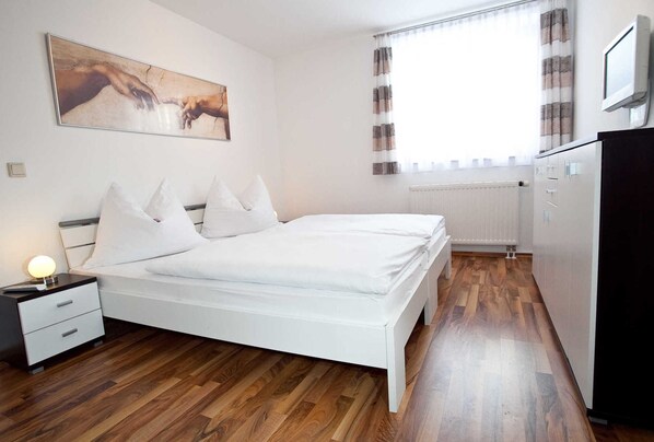 Un dormitorio con cama, mesita de noche, lámpara y un cuadro en la pared.