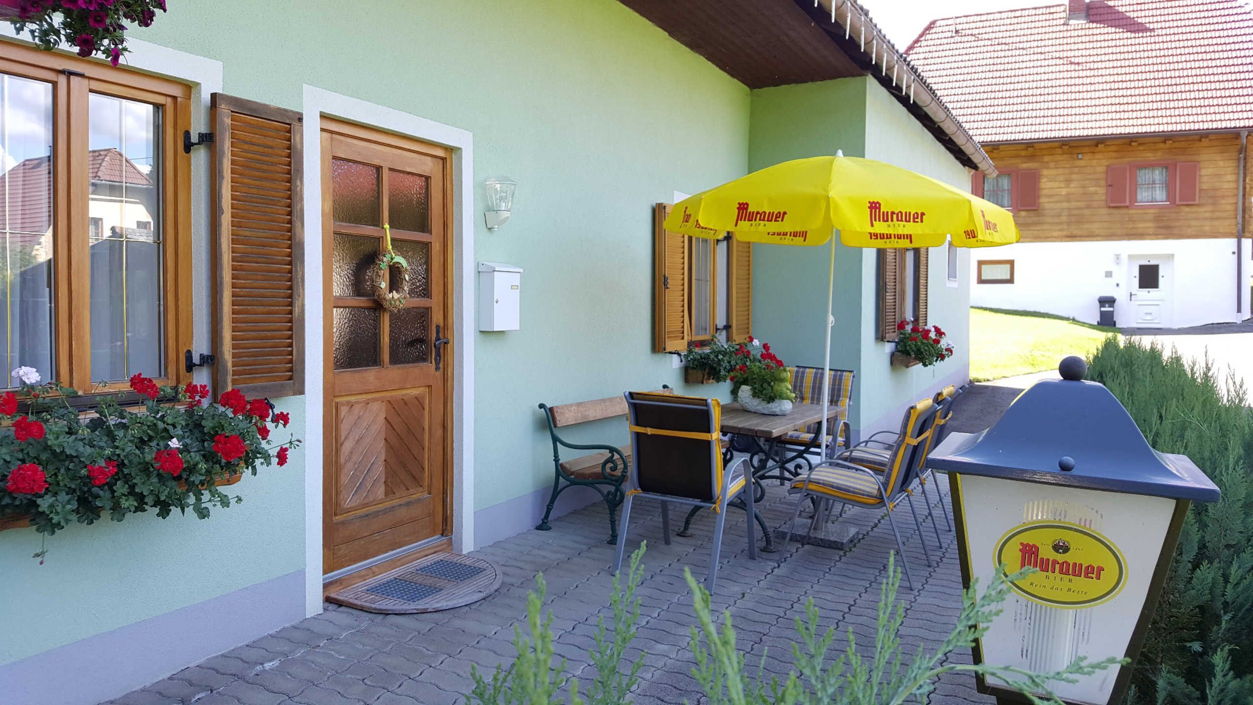 Un bâtiment avec une porte en bois, un banc, une table et un parapluie jaune.