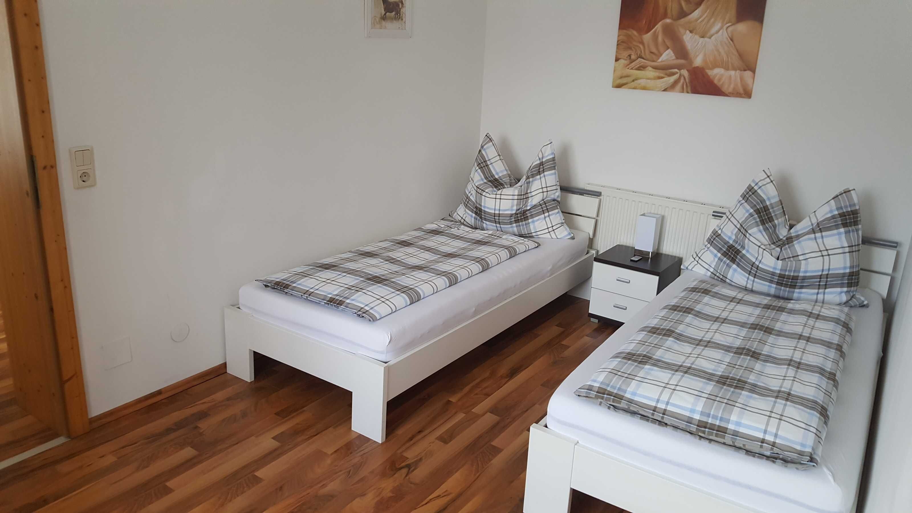 A small, clean room with two single beds, a nightstand with a lamp, and a radiator.