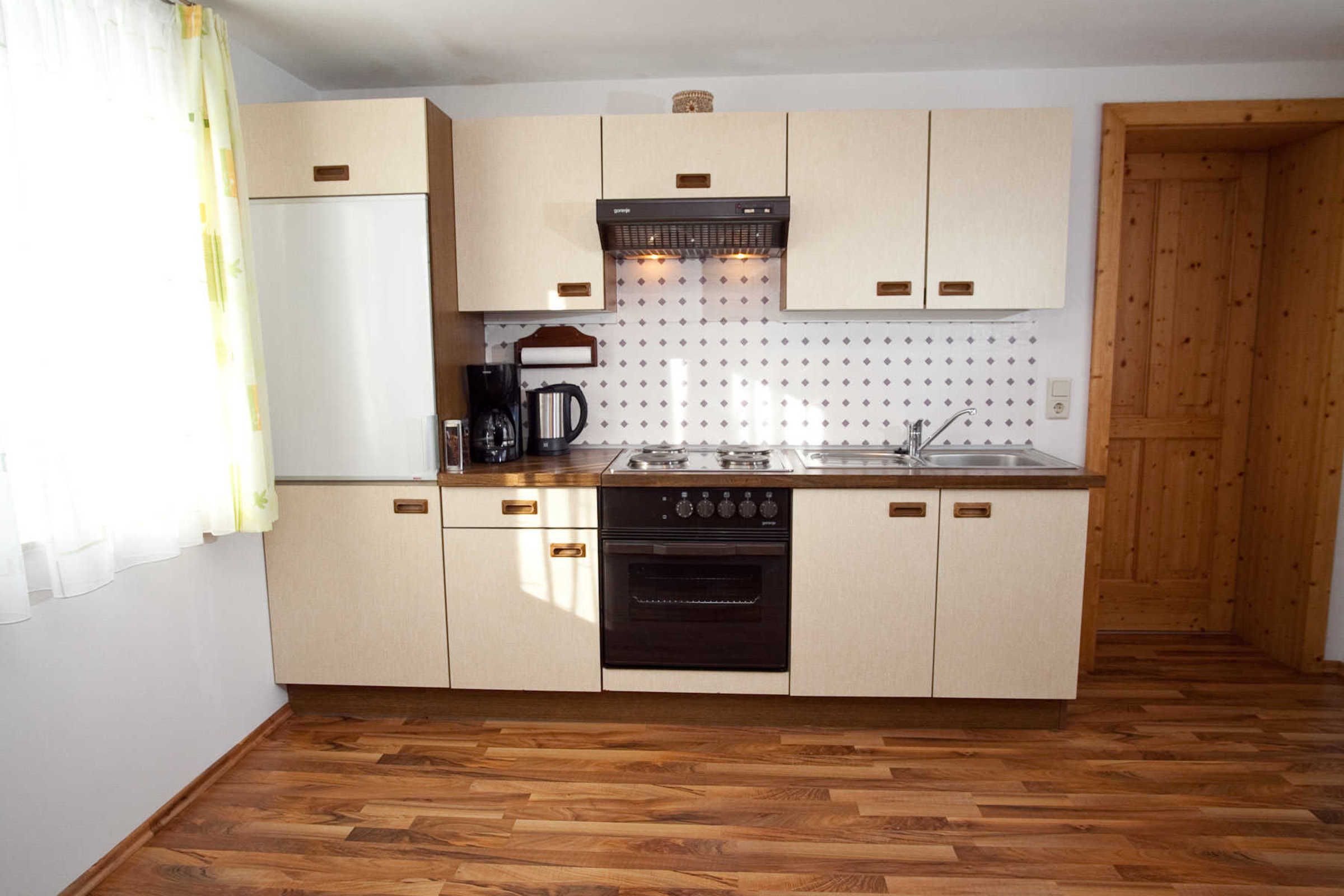 Cocina compacta con armarios de madera, horno integrado, cafetera y lavabo.