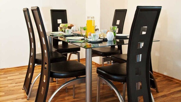 A dining area with a glass table, four black chairs, and two wall-mounted paintings. - Holiday home Findling Summer - House Findling (Sankt Lambrecht)