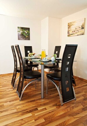 Un coin repas avec une table en verre, quatre chaises noires et deux tableaux accrochés au mur.