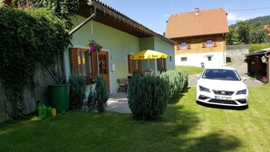 A house with a car parked in front, a small outdoor seating area, and a green lawn. - Holiday home Findling Summer - House Findling (Sankt Lambrecht)