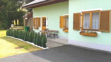 Um edifício de dois andares com fachada verde, persianas de madeira e entrada pavimentada.