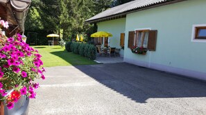 A building with a paved driveway, outdoor seating area with yellow umbrellas, and flower boxes on the wall. - Holiday home Findling Summer - House Findling (Sankt Lambrecht)