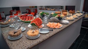 Un bufé con diversos alimentos, entre ellos sandía, queso y pan.