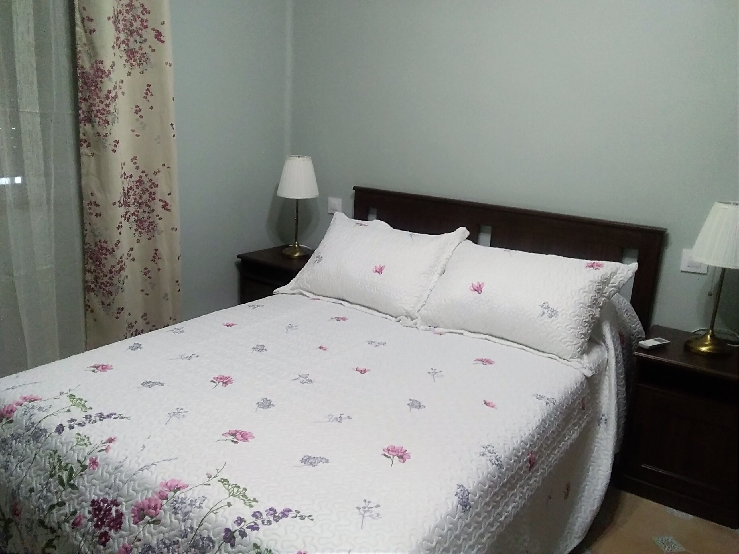 Een keurig opgemaakt bed met bloemenbedrukking, een bedlamp en een nachtkastje.