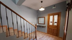 Un escalier doté d’une rampe en bois et de balustres noires, menant à un palier où se trouvent un miroir et une porte à panneaux de verre.