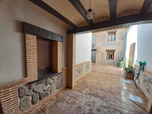 A spacious courtyard with a wooden floor, stone walls, and a brick building in the background. - A rural house with the comforts of the city (Socuéllamos)