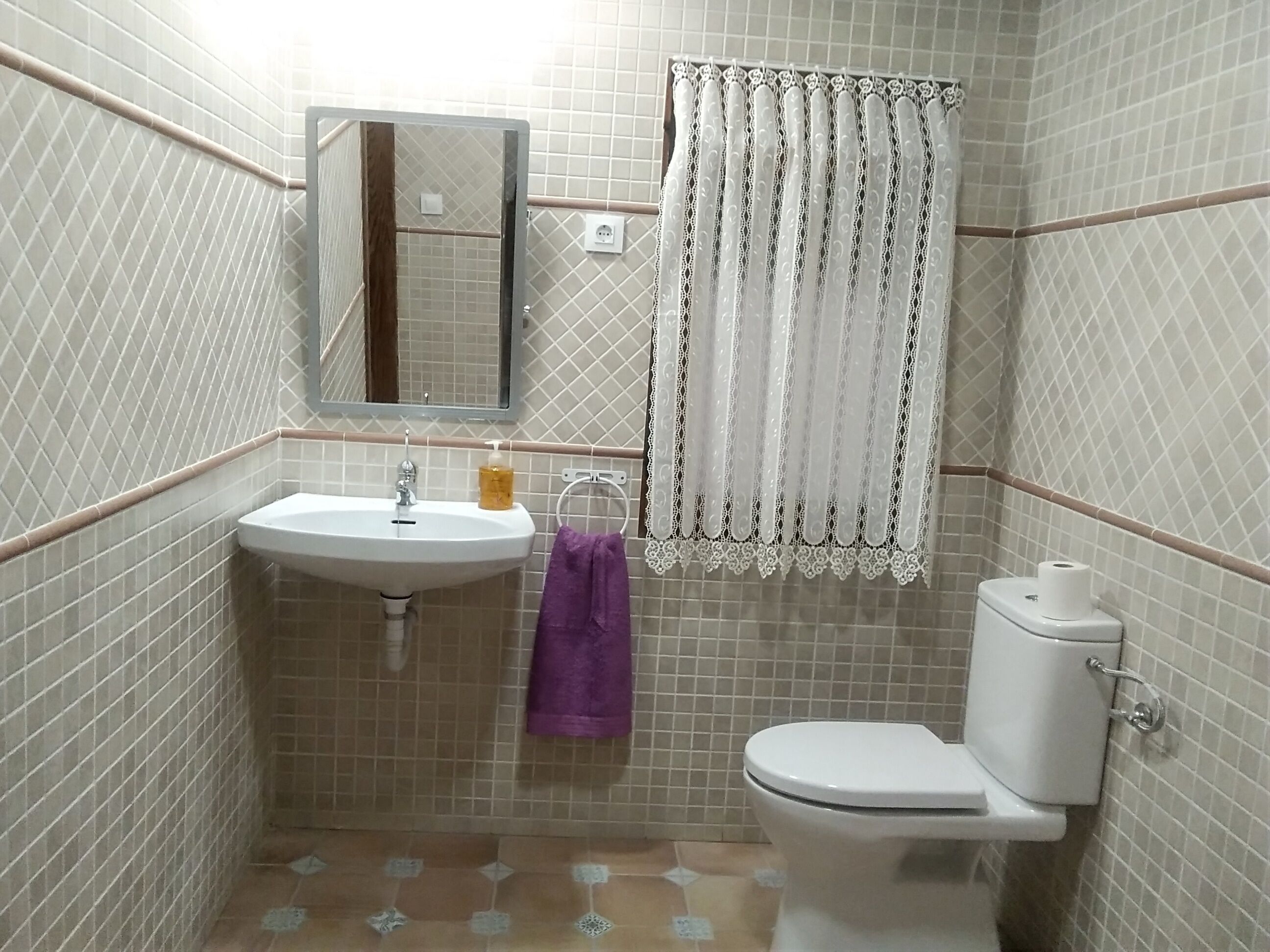 Een badkamer met een wastafel, spiegel, toilet en betegelde wanden.