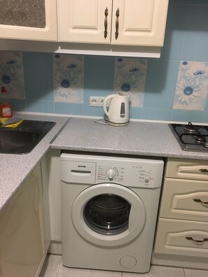 A compact kitchen with a washing machine, a kettle, and a sink.
