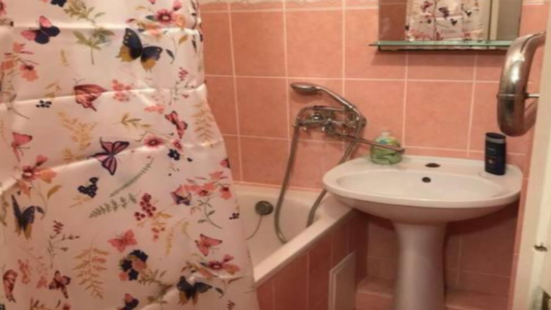 A bathroom with a floral shower curtain, a white sink, and a handheld showerhead.