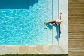 Eine Person entspannt am Pool mit klarem Wasser, einer Holzterrasse und einer Steinmauer.