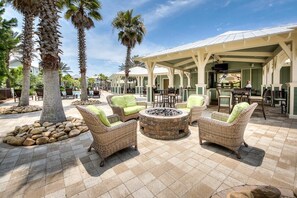 An outdoor seating area with wicker furniture and a fire pit, surrounded by palm trees and a covered patio. - 3,000+ Sq Ft! 5 Bikes! 3 King Suites- Serenity Pond at NatureWalk on 30A (Santa Rosa Beach)