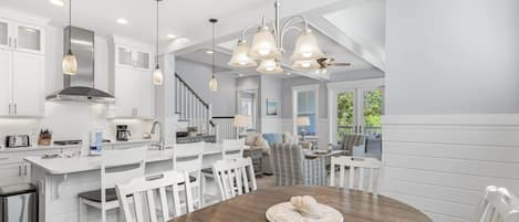 A modern kitchen with white cabinetry, a wooden dining table, and pendant lighting.