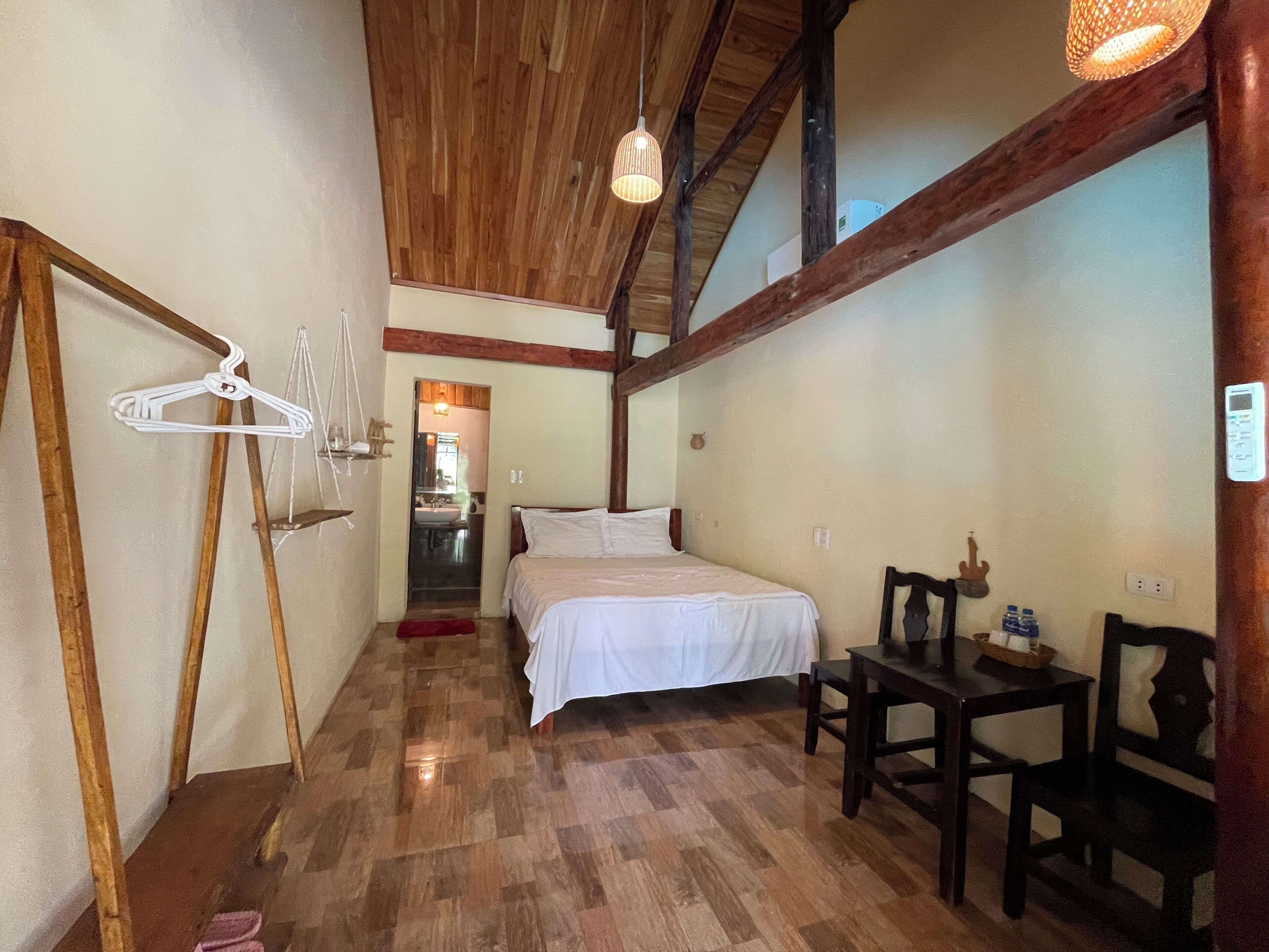 Un dormitorio con piso de madera, una cama, una mesa con sillas y una lámpara colgante.