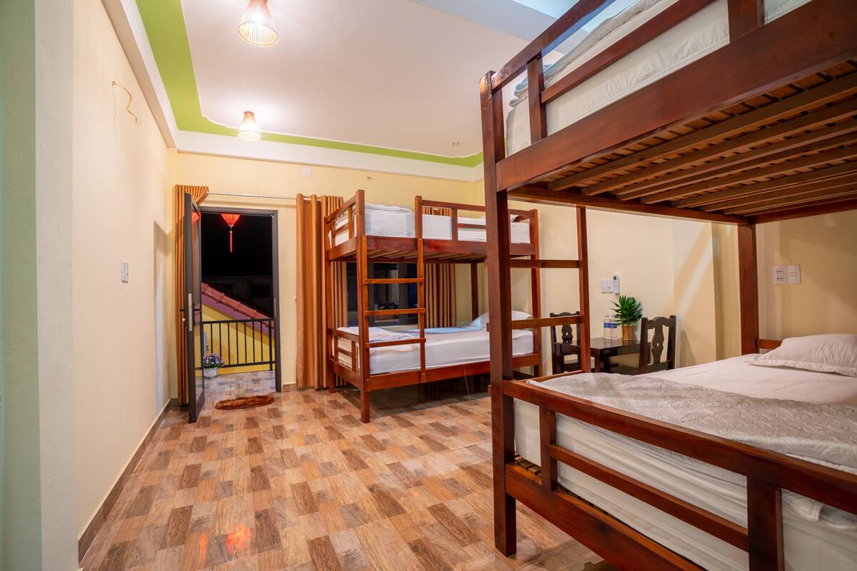 A room with three bunk beds, a small table with a plant, and a staircase leading to another level.