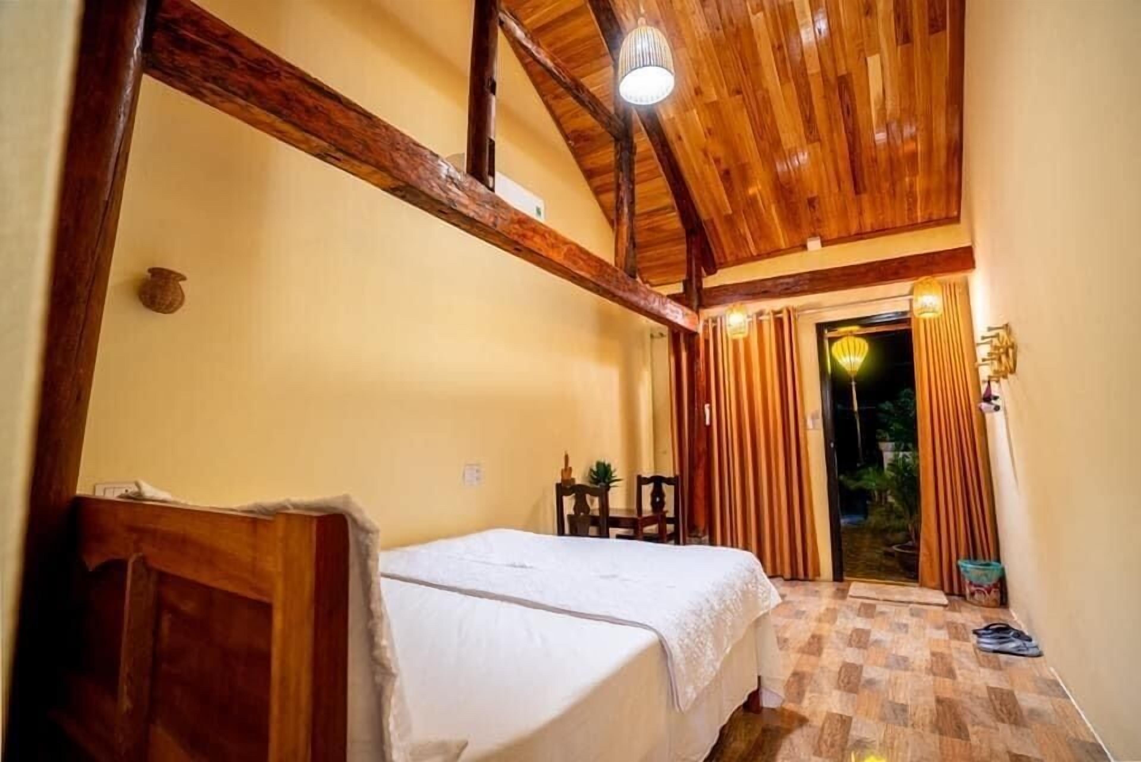 A room with a wooden ceiling, a bed, a chair, and a door leading to an outdoor area.