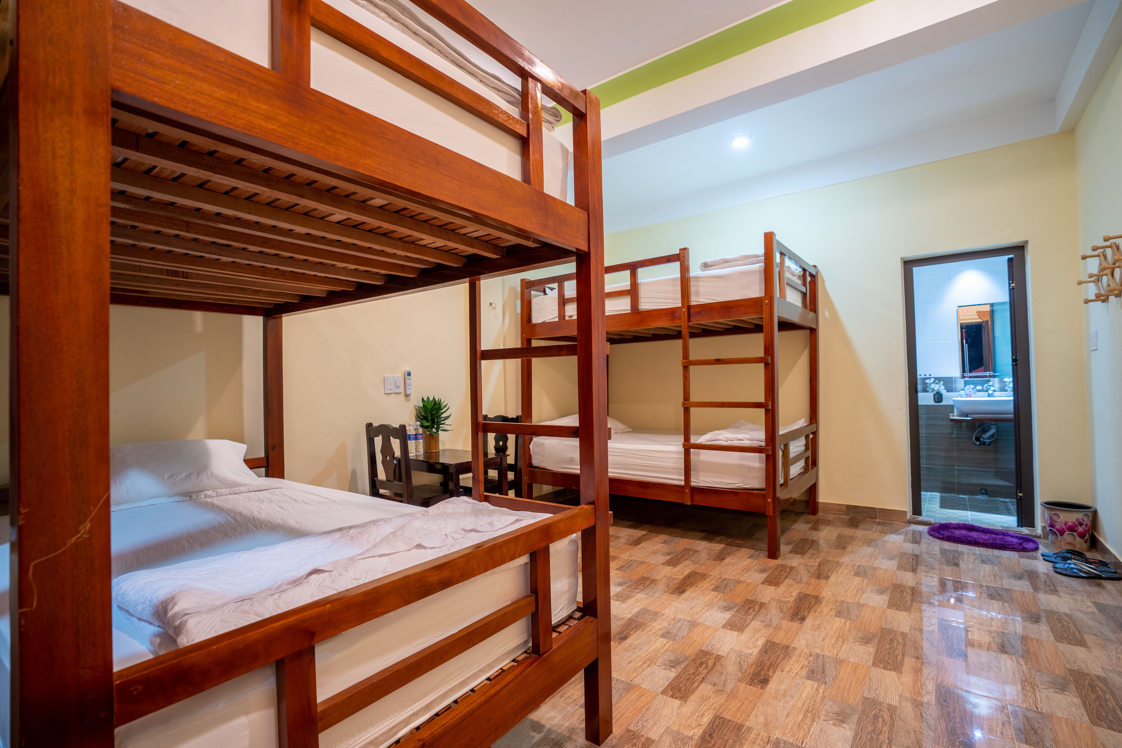 Una habitación con tres literas, una mesita con una planta, y se ve una puerta de baño al fondo.