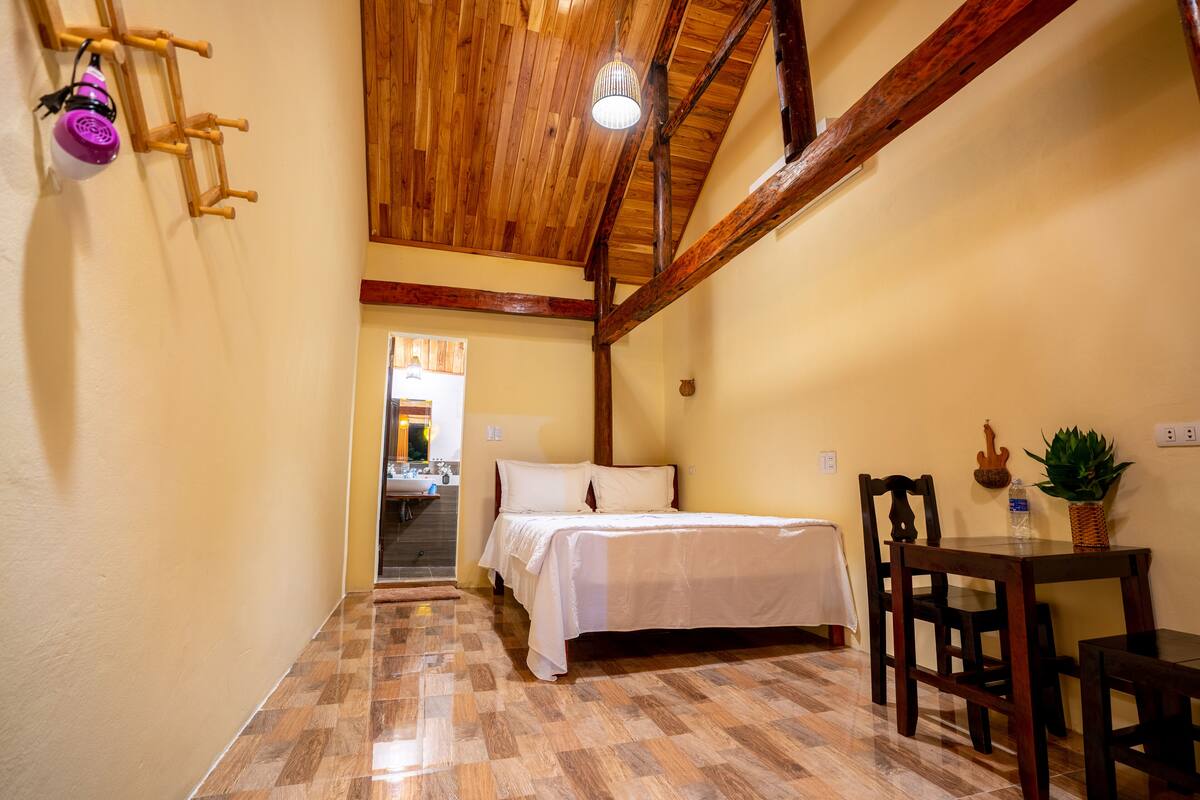 A bedroom with a wooden ceiling, a bed, a table, and chairs.
