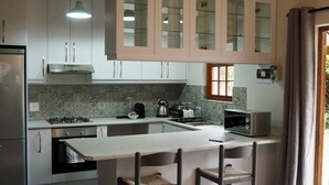 A modern kitchen with white cabinets, a central island, and a dining area with a sofa and chairs. - Self Catering Fully Equipped Cottage set in a leafy suburb (Plumstead)