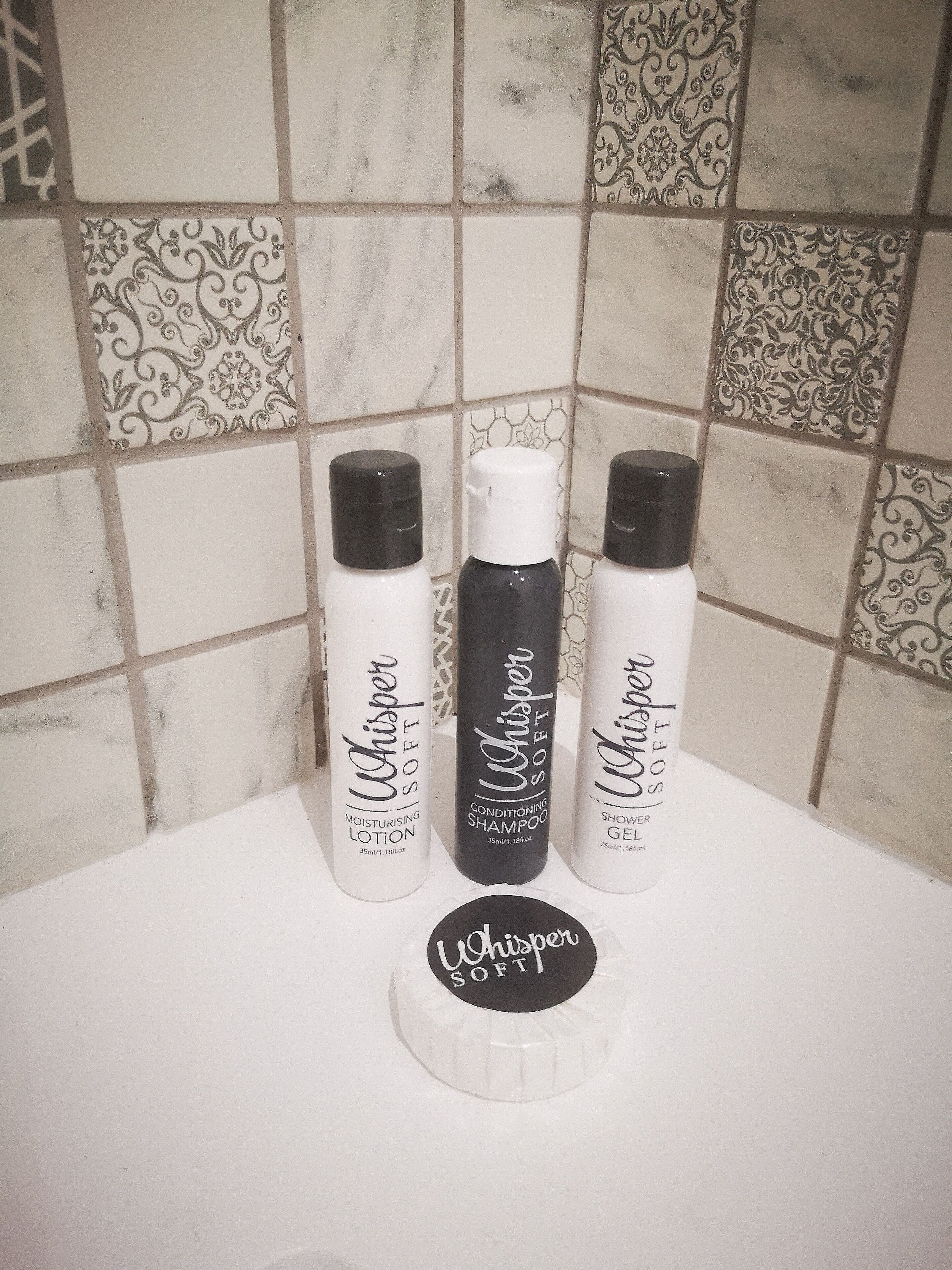Drei Flaschen Whisper Soft Produkte auf einer Badezimmerablage.