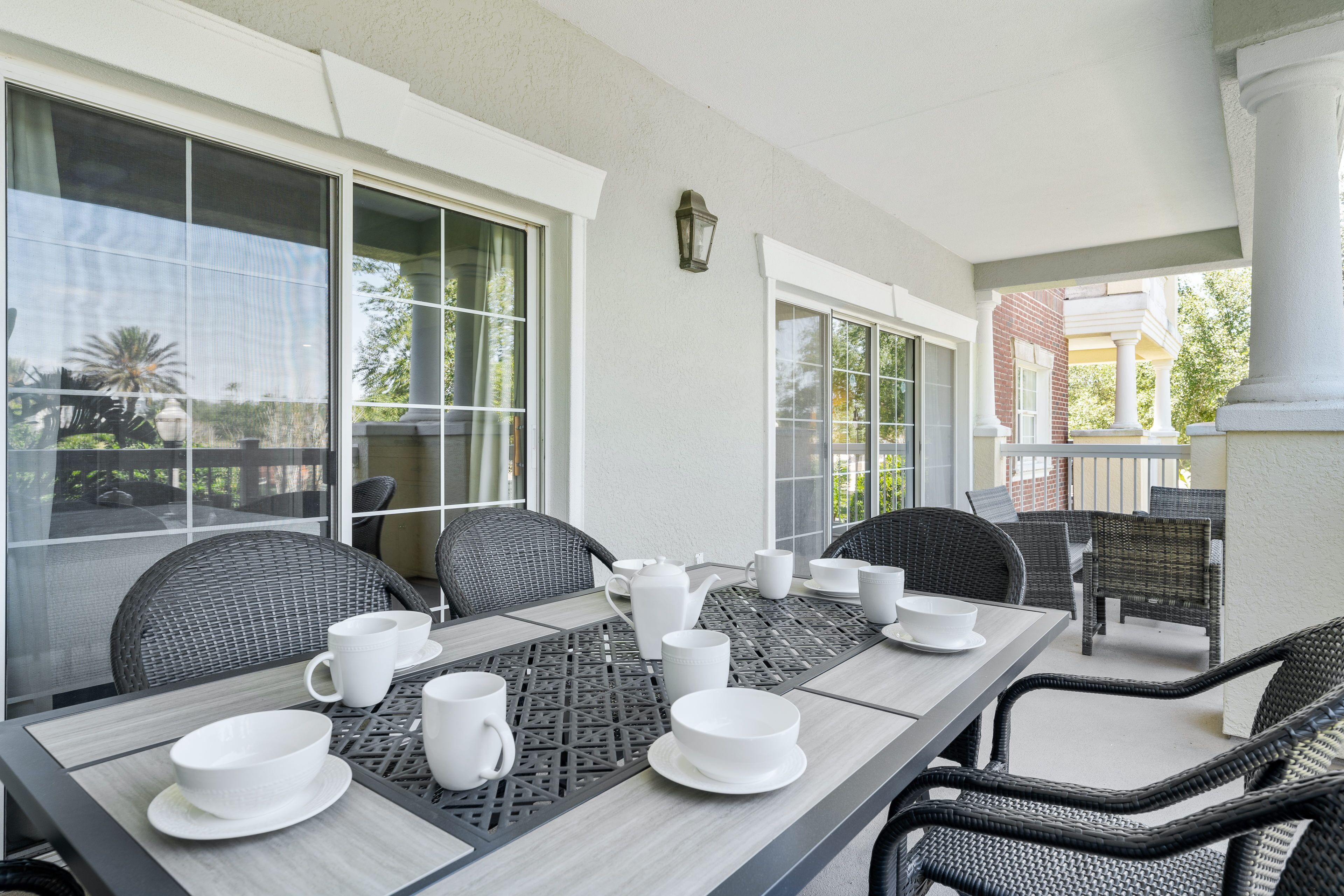 A dining area with a table set for four, surrounded by wicker chairs, large windows, and a view of a building in the background.