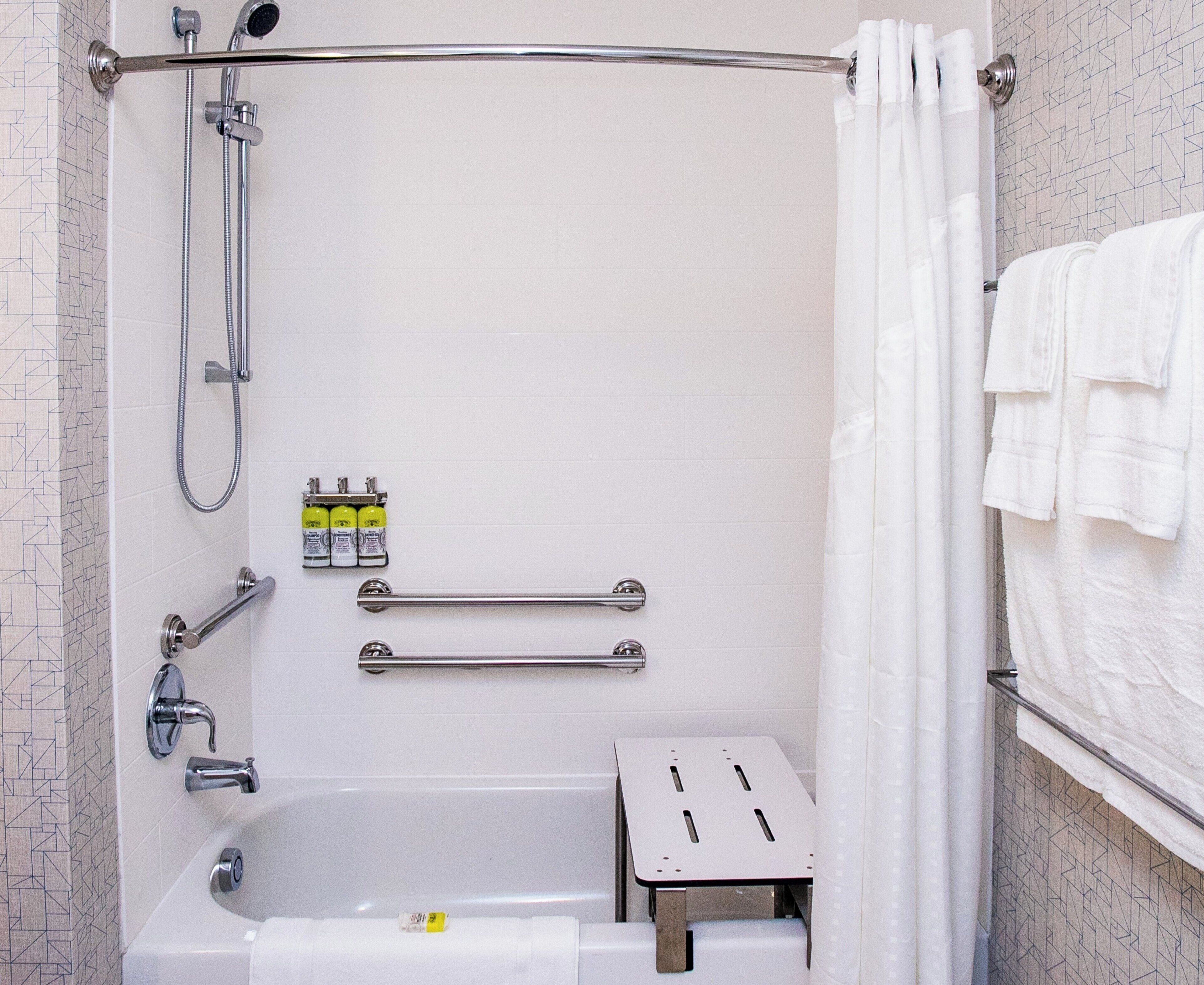 A shower with a handheld showerhead, a handheld shower attachment, a handheld shower hose, a grab bar, a towel rack, and a small step stool.