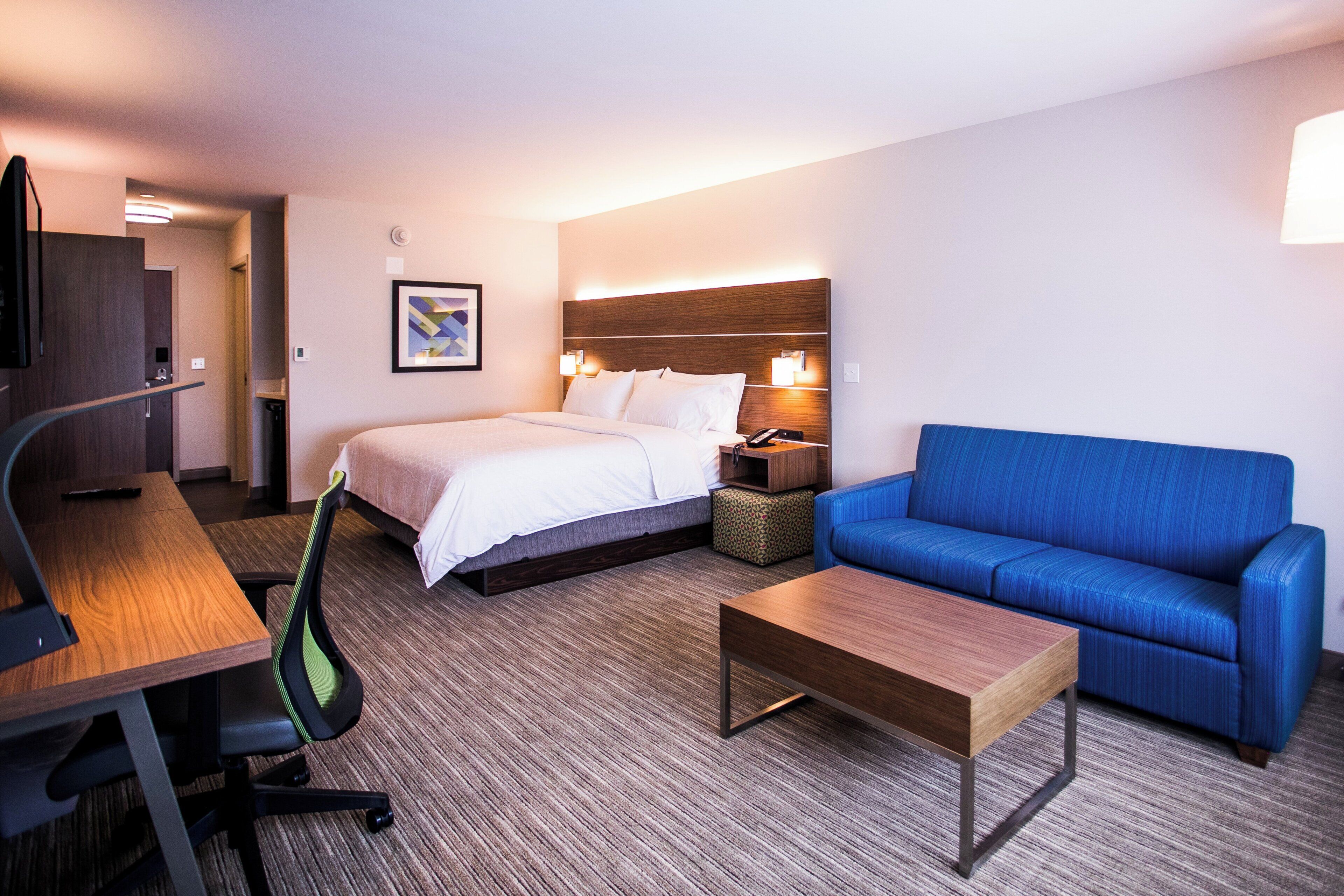 A hotel room with a bed, a desk, a blue sofa, a small table, and a TV.