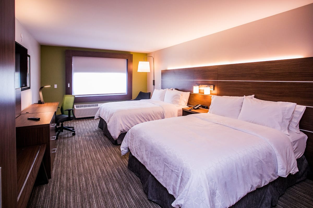 A hotel room with two beds, a desk, a chair, a TV, and a window with blinds.