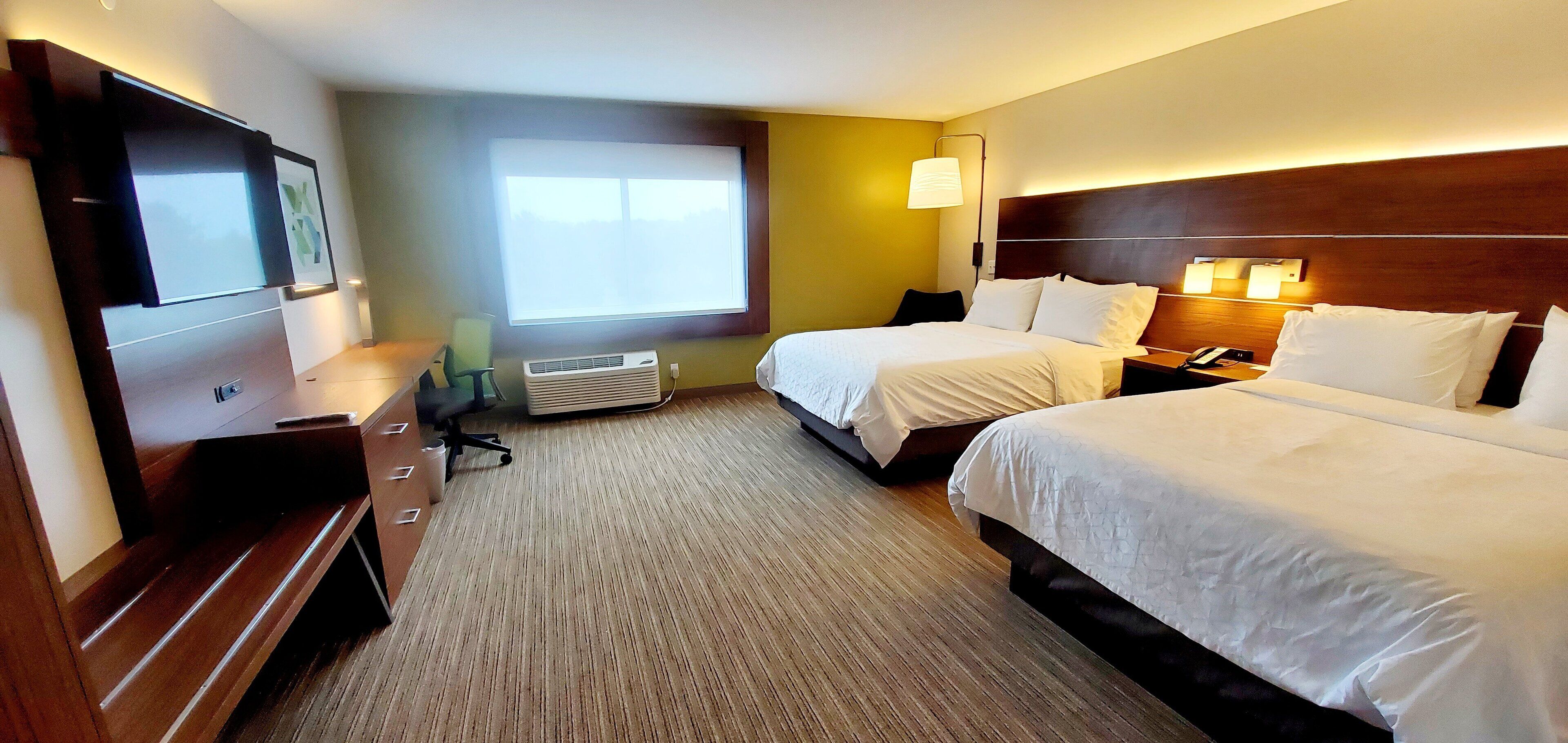 A hotel room with two beds, a desk, a chair, a TV, and a window.