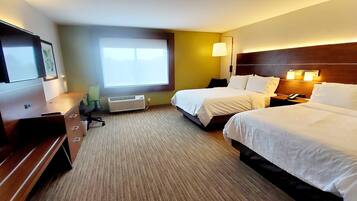 A hotel room with two beds, a desk, a chair, a TV, and a window.