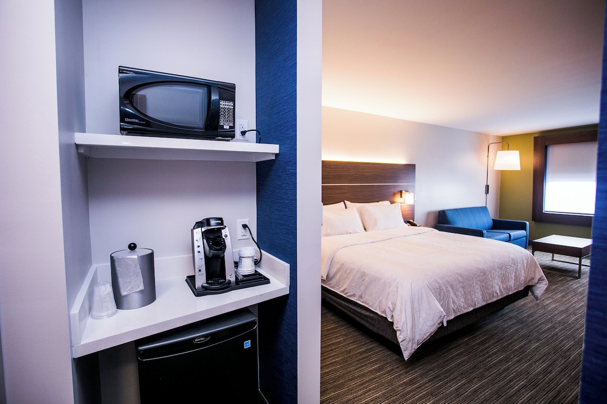 A hotel room with a bed, a desk with a microwave, a coffee maker, and a lamp.
