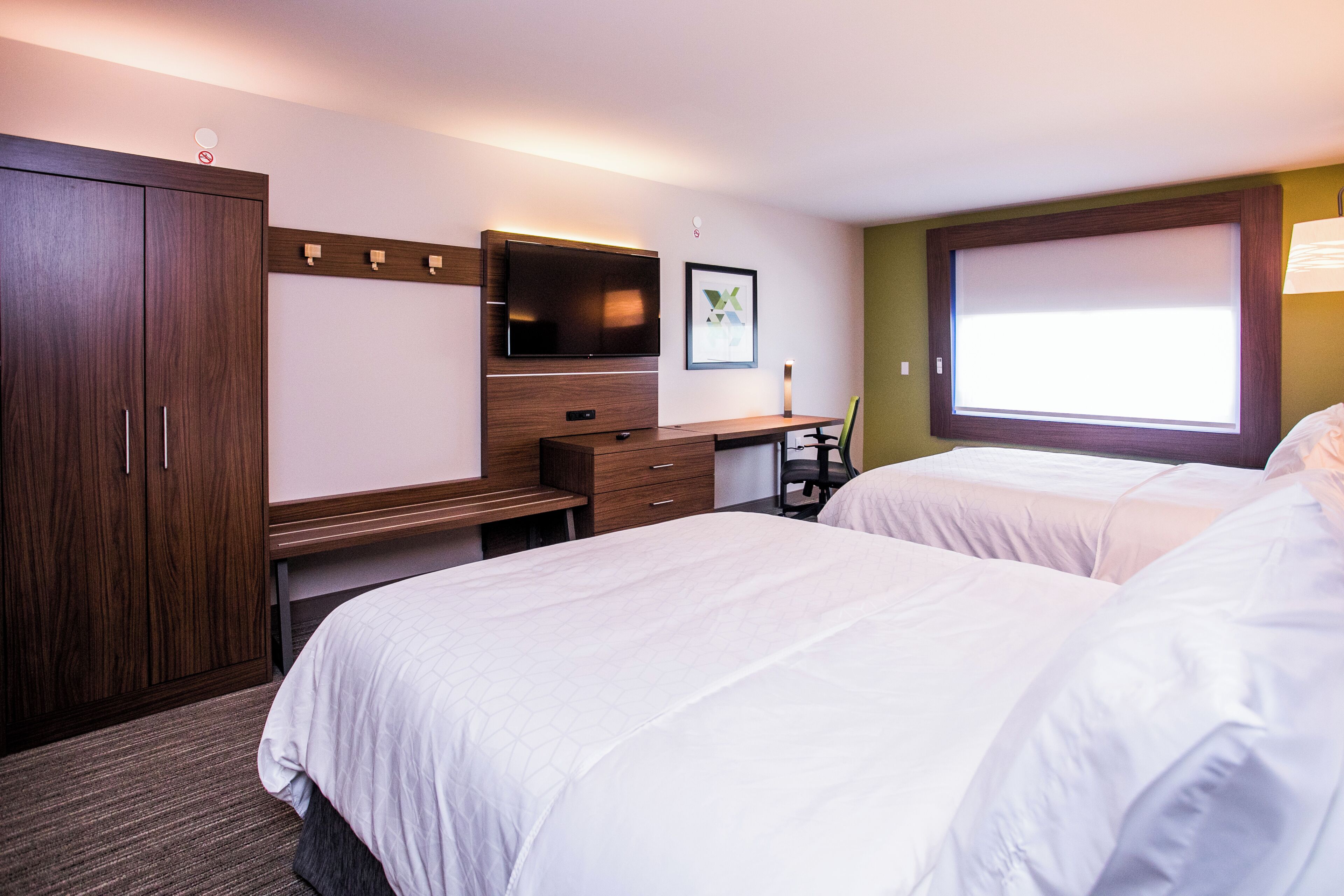 Quarto de hotel com duas camas, uma escrivaninha, uma televisão e uma janela.