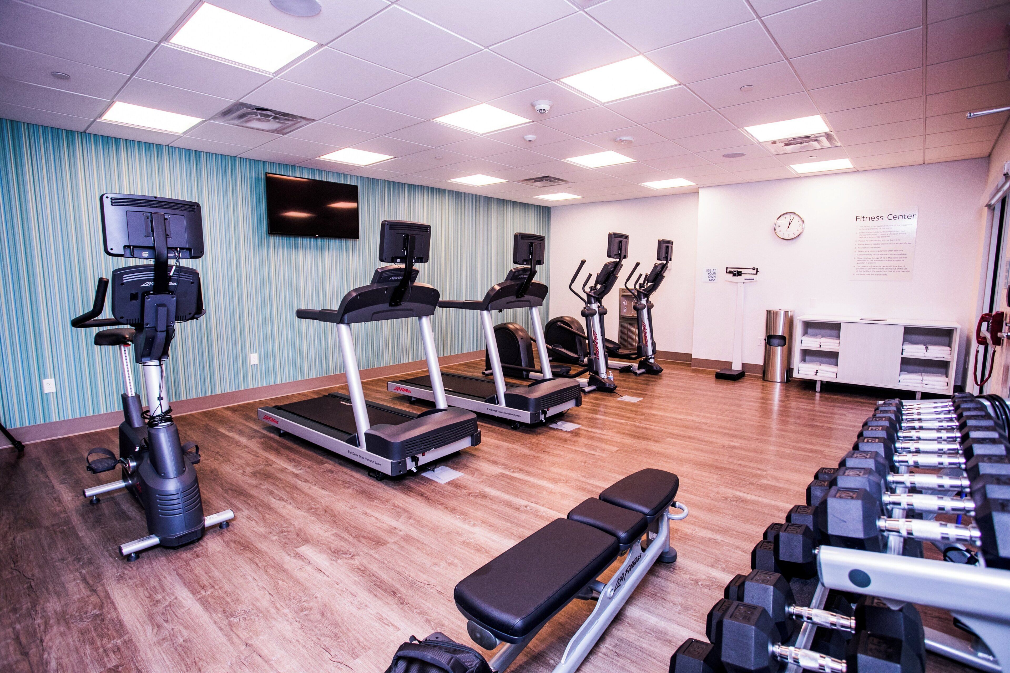 Un gimnasio con cintas de correr, elípticas, una banca y pesas.