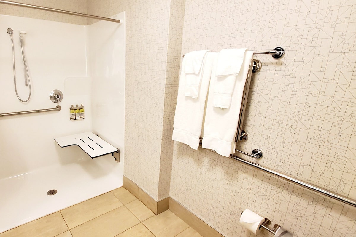 A shower area with a glass door, a towel rack with towels, and a handrail.