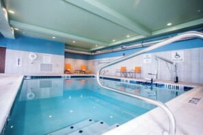 An indoor swimming pool with clear lane markings, a pool lift, and lounge chairs.